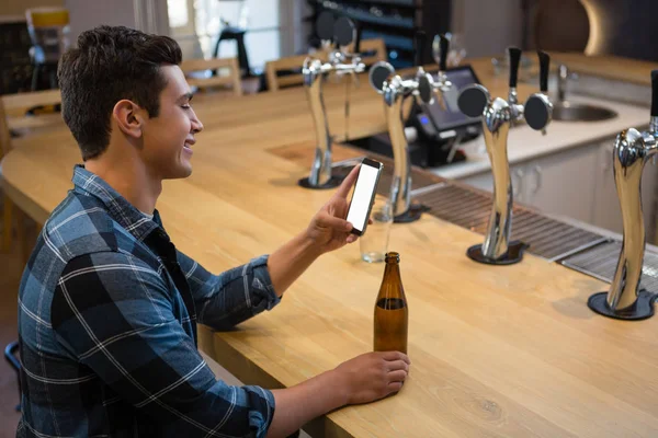 Muž s pivní lahví pomocí telefonu na baru — Stock fotografie