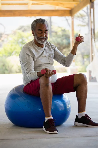 Homem sênior exercitando com halteres em bola de exercício — Fotografia de Stock