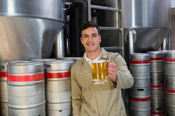 Homem segurando vidro de cerveja contra tanques de armazenamento — Fotografia de Stock