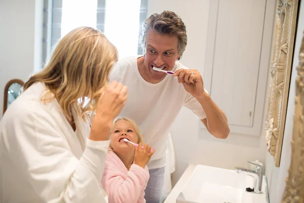 Родители и дочь чистят зубы в ванной комнате — стоковое фото