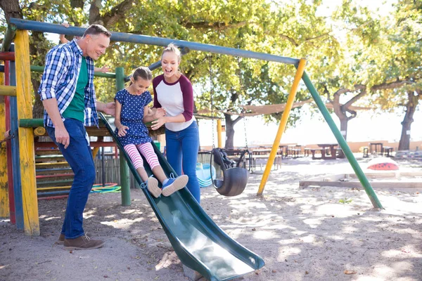 Padres mirando hija jugando en diapositiva — Foto de Stock