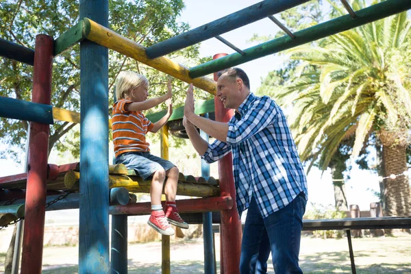 Father giving high five to son sitting on jungle gym — Stock Photo, Image