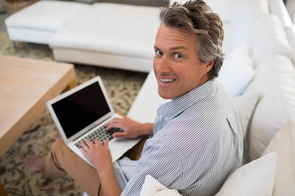 Uomo sorridente utilizzando il computer portatile in soggiorno — Foto Stock