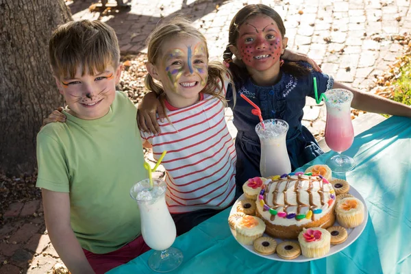 Amigos con pintura facial sentados junto a la comida y la bebida —  Fotos de Stock