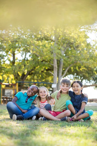 Barn med armar runt sitter på park — Stockfoto