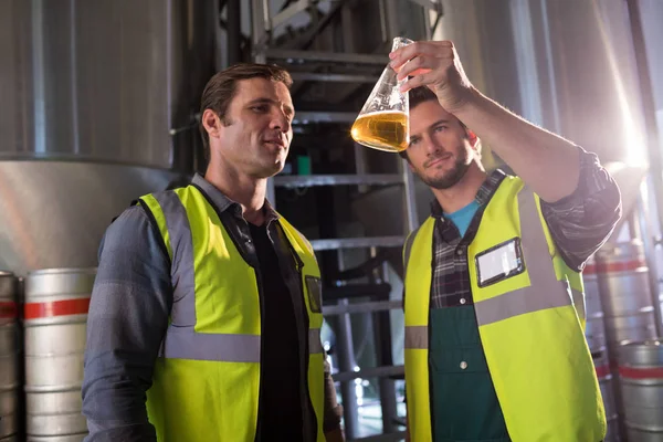 Compañeros de trabajo examinando cerveza en vaso de precipitados — Foto de Stock