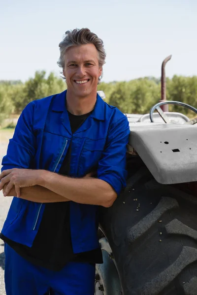 Travailleur penché avec les bras croisés près du tracteur — Photo