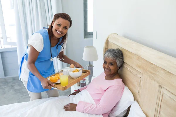Médico femenino que sirve el desayuno a la mujer mayor —  Fotos de Stock