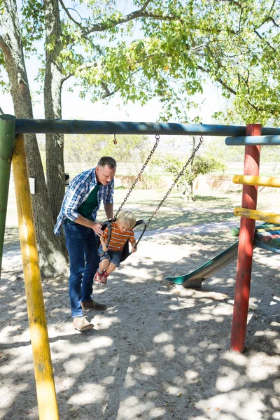 Padre empujando hijo sentado en swing — Foto de Stock