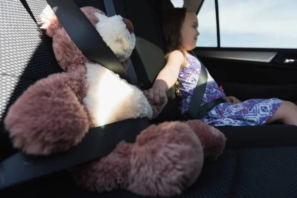 Menina sentada com ursinho de pelúcia no banco de trás do carro — Fotografia de Stock