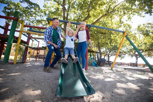 Ouders kijken naar zoon glijden op speelplaats — Stockfoto