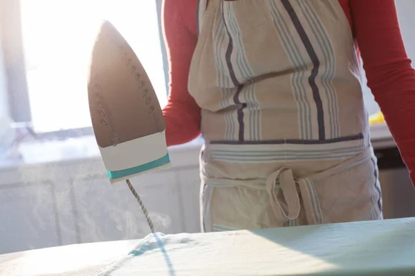 Vrouw strijken shirt op strijkplank in keuken — Stockfoto