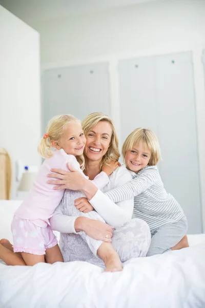 Kinder umarmen ihre Mutter im Schlafzimmer — Stockfoto