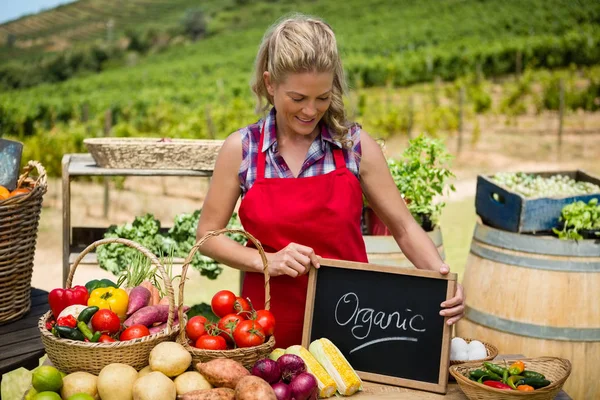 Happy woman holding slate with text at vegetable stall — Stock Photo, Image