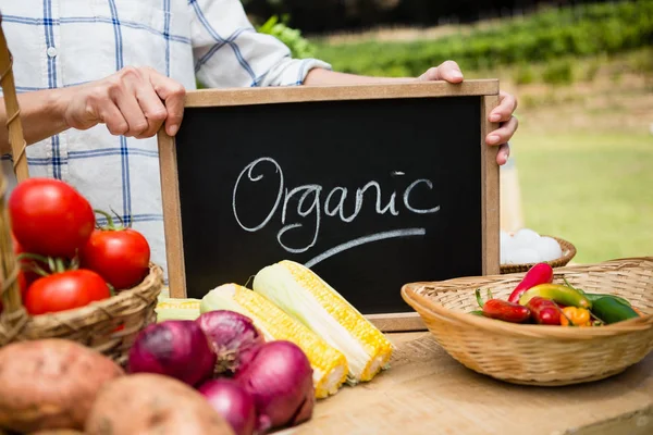 Mujer sosteniendo pizarra con texto en puesto de verduras — Foto de Stock