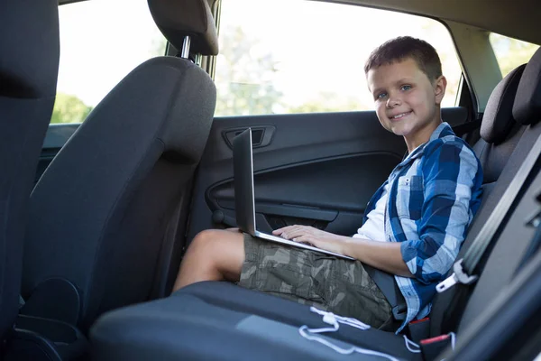 Genç çocuk arabanın arka koltuğunda dizüstü bilgisayar kullanarak — Stok fotoğraf