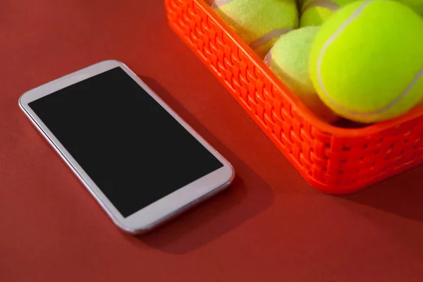 Tennis balls in red basket by smartphone — Stock Photo, Image