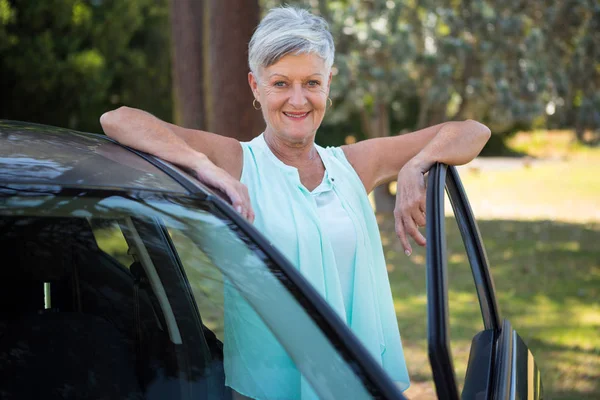 Senior woman standing beside a car — Stock Photo, Image