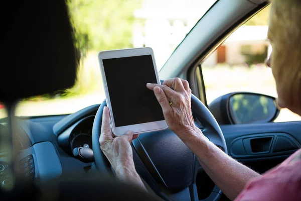Старшая женщина, использующая цифровой планшет в машине — стоковое фото