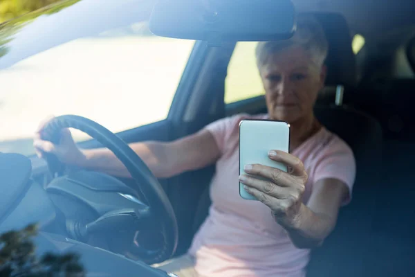 Senior vrouw met behulp van de telefoon tijdens het auto rijden — Stockfoto