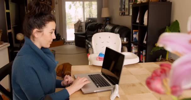 Vrouw die aan de keukentafel met behulp van laptop zit — Stockvideo