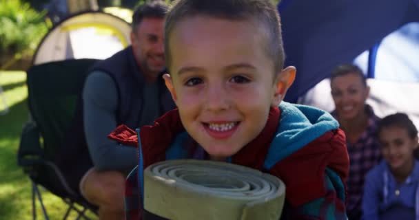 Niño sosteniendo una estera enrollada mientras la familia está sentada en la tienda — Vídeos de Stock
