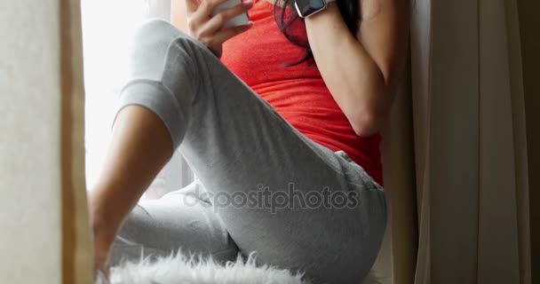 Mujer sentada en el alféizar de la ventana y usando el teléfono móvil — Vídeos de Stock
