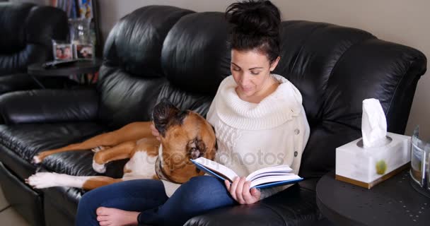 Mujer leyendo una novela mientras perro relajándose en su regazo — Vídeos de Stock