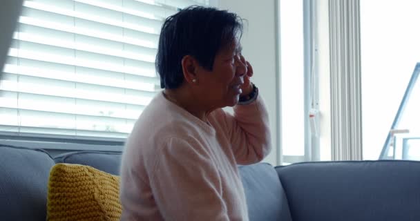 Старшая женщина разговаривает по мобильному телефону в гостиной — стоковое видео