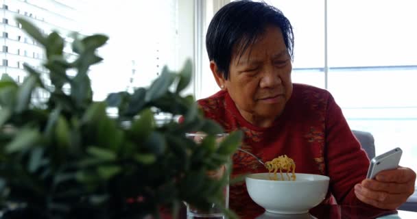 Mujer mayor usando el teléfono móvil mientras tiene comida — Vídeo de stock