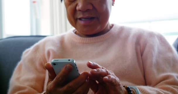 Ηλικιωμένη γυναίκα που χρησιμοποιεί κινητό τηλέφωνο στο σαλόνι — Αρχείο Βίντεο
