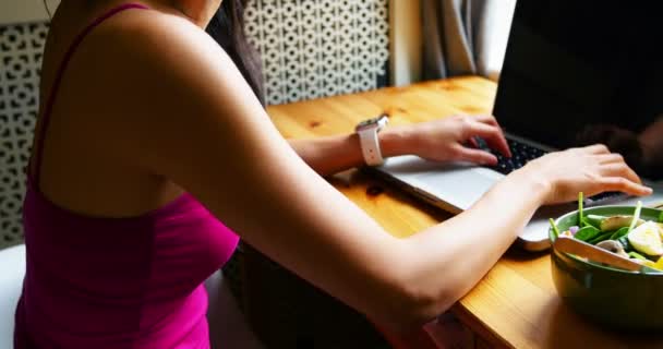Femme utilisant un ordinateur portable tout en prenant le petit déjeuner — Video