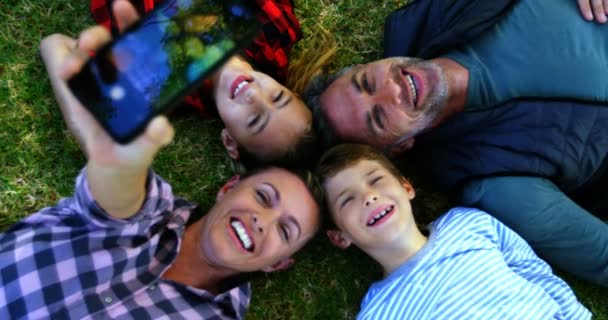 Famille heureuse allongée sur l'herbe et prenant selfie — Video