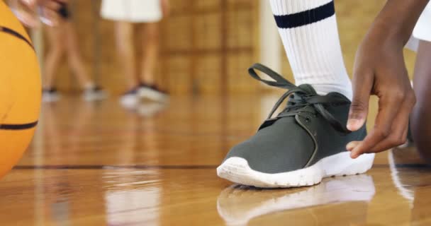 Niño de secundaria atando cordones de zapatos en cancha de baloncesto — Vídeos de Stock