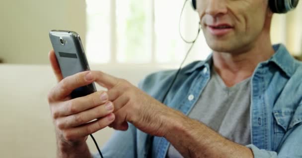 Man lyssnar musik på mobilen i vardagsrum — Stockvideo