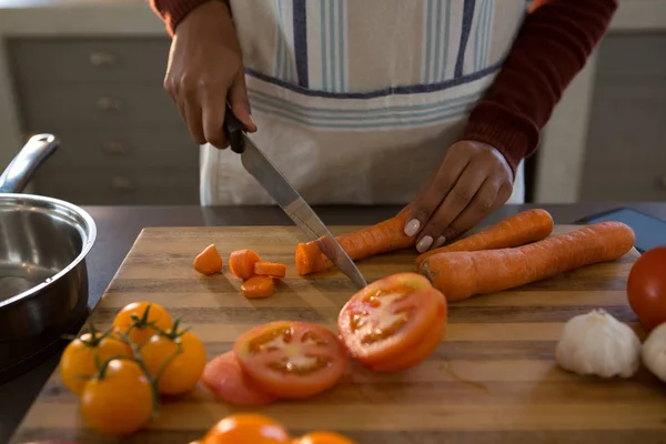 Woman cutting carrot at counter — Stock Photo, Image