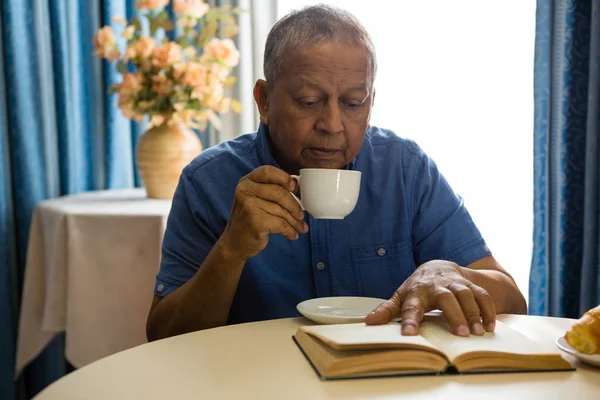 Pria senior minum sambil membaca buku — Stok Foto