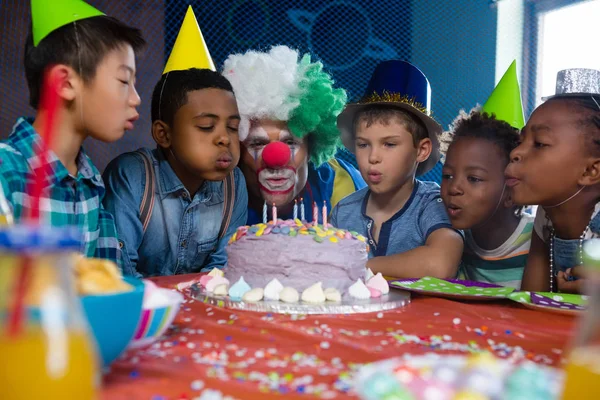 Enfants avec clown soufflant des bougies sur le gâteau — Photo