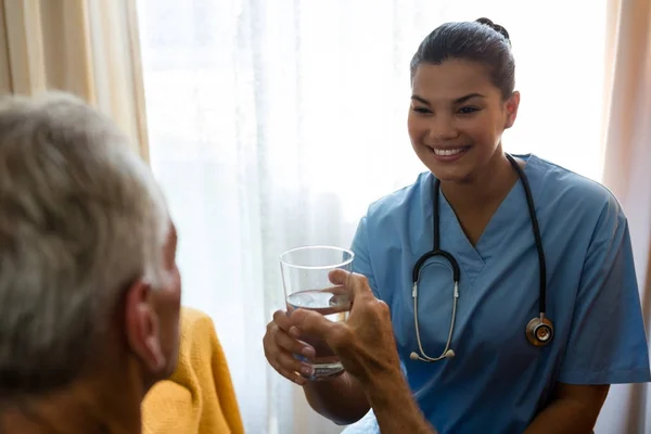 Vrouwelijke arts water geven senior man — Stockfoto