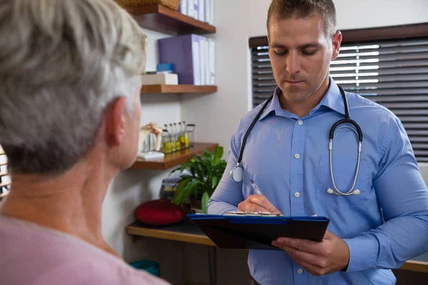 Physiotherapist writing prescription on clipboard for patient — Stock Photo, Image