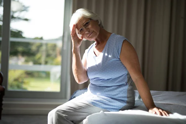 Tense senior woman sitting on bed in bedroom — Stock Photo, Image