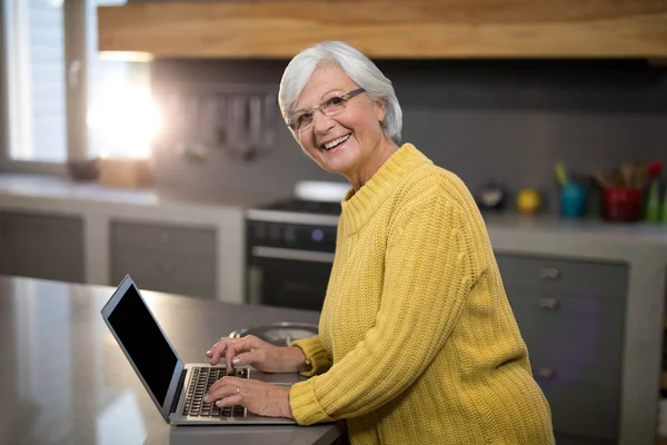 Mujer mayor usando portátil en la cocina —  Fotos de Stock