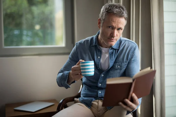 Чоловік читає книгу, маючи каву — стокове фото