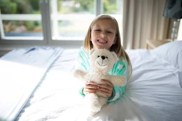 Mädchen hält Teddybär auf Bett im Schlafzimmer — Stockfoto