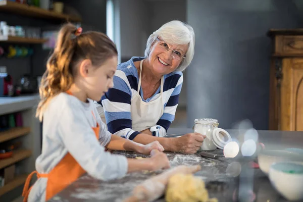 Granddaughter flattening dough with grandmother — Stock Photo, Image