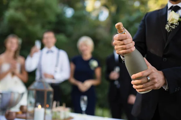 Groom opening champagne bottle at park — Stock Photo, Image