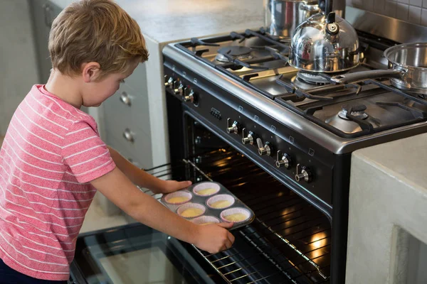 Boy holding muffin tin by oven in kitchen — Stock Photo, Image