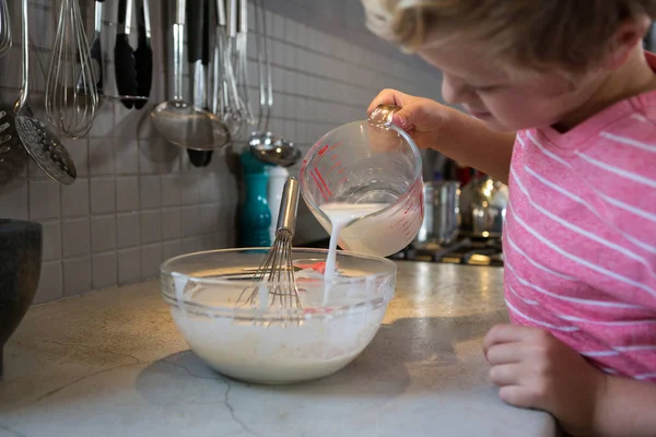 Boy pouring milk in batter — Stock Photo, Image