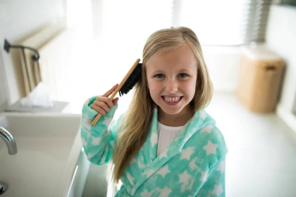 Smiling girl combing her hair in bathroom — Stock Photo, Image