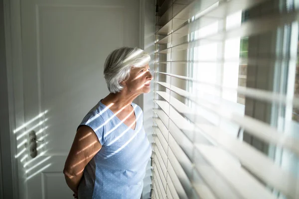 Старшая женщина смотрит в окно в спальне — стоковое фото